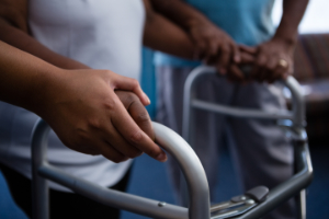 Woman being assisted while walking with a mobility walker.